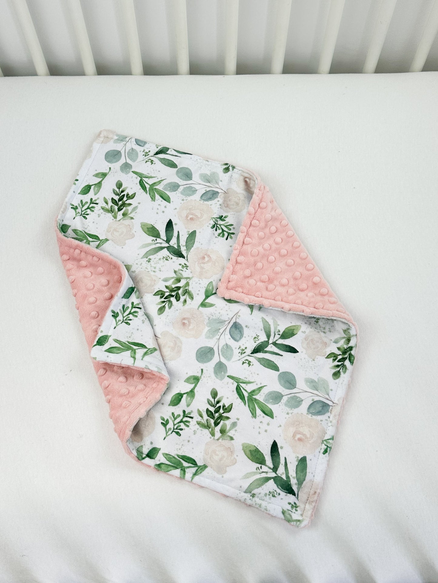 a white crib with a pink and green floral blanket
