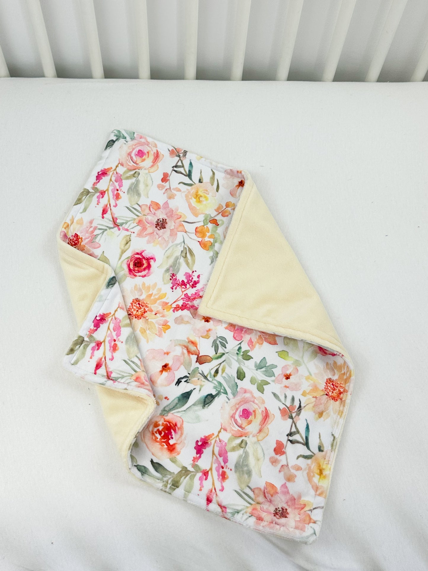 a white crib with a flowered blanket and a white crib rail