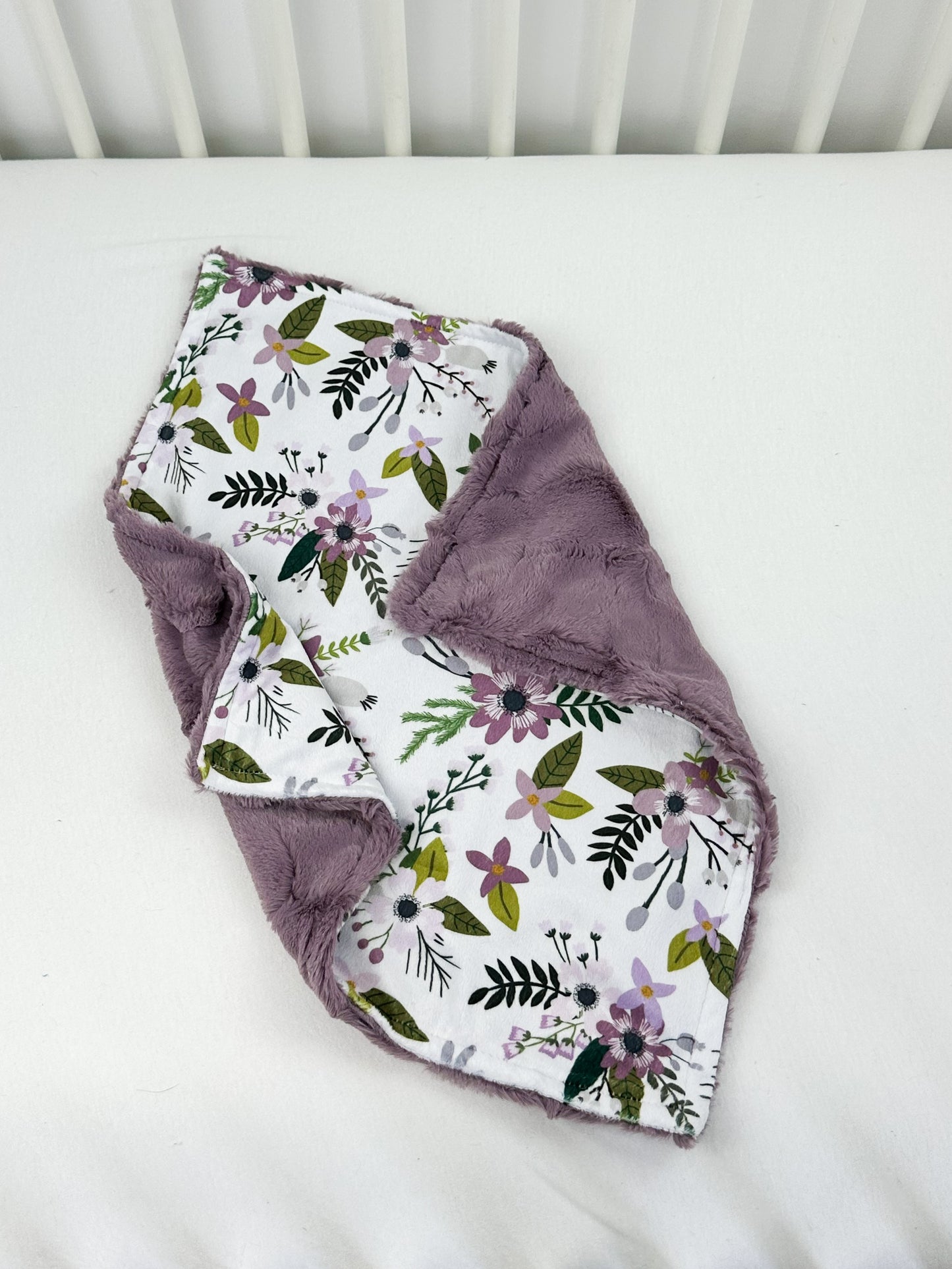 a white crib with a purple flowered blanket on top of it