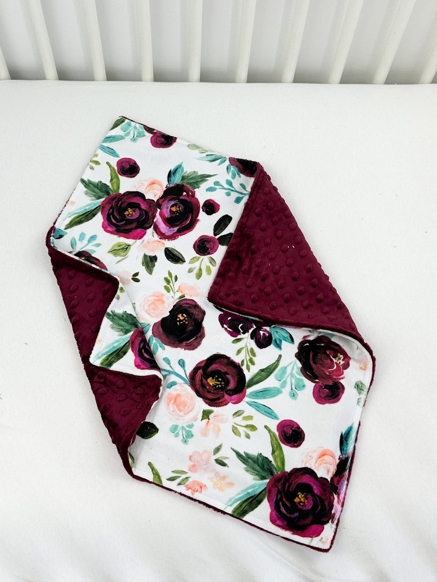 a white crib with a red and purple flowered blanket on top of it