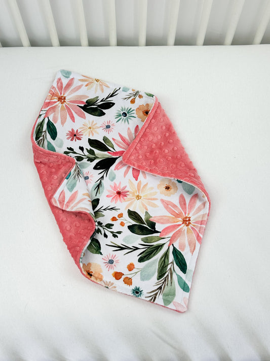 a baby's crib with a pink and green flowered blanket