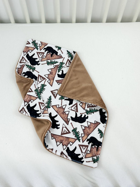 a baby blanket with a bear and trees on it