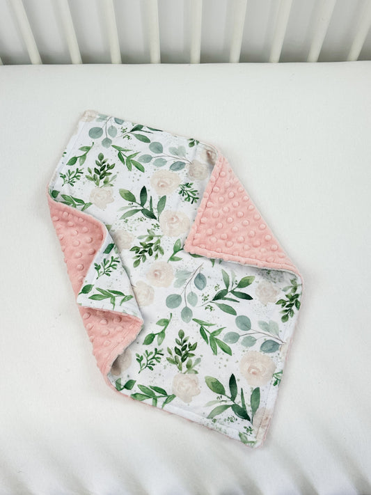 a white crib with a pink and green floral blanket