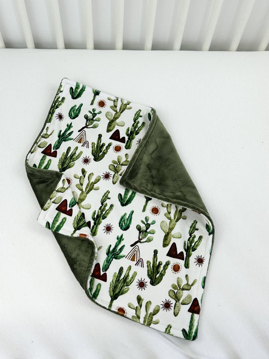 a white crib with a green and white blanket and a green and white cactus