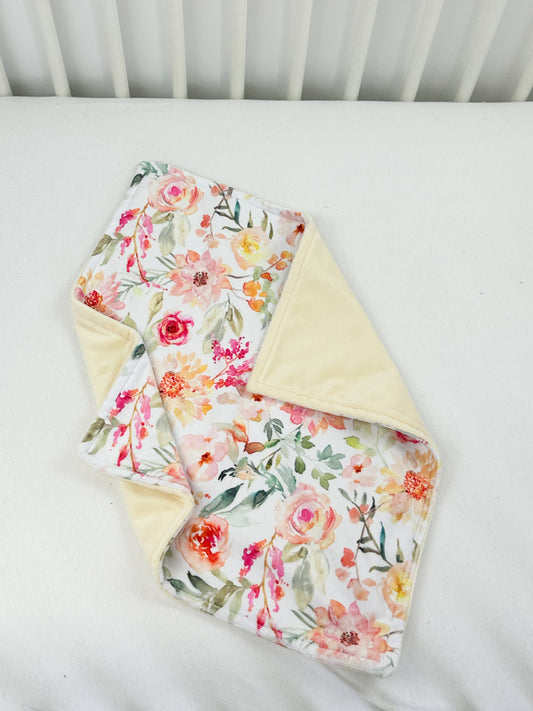 a white crib with a flowered blanket and a white crib rail