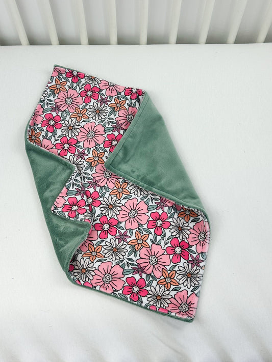 a pink and green flowered blanket on a white crib