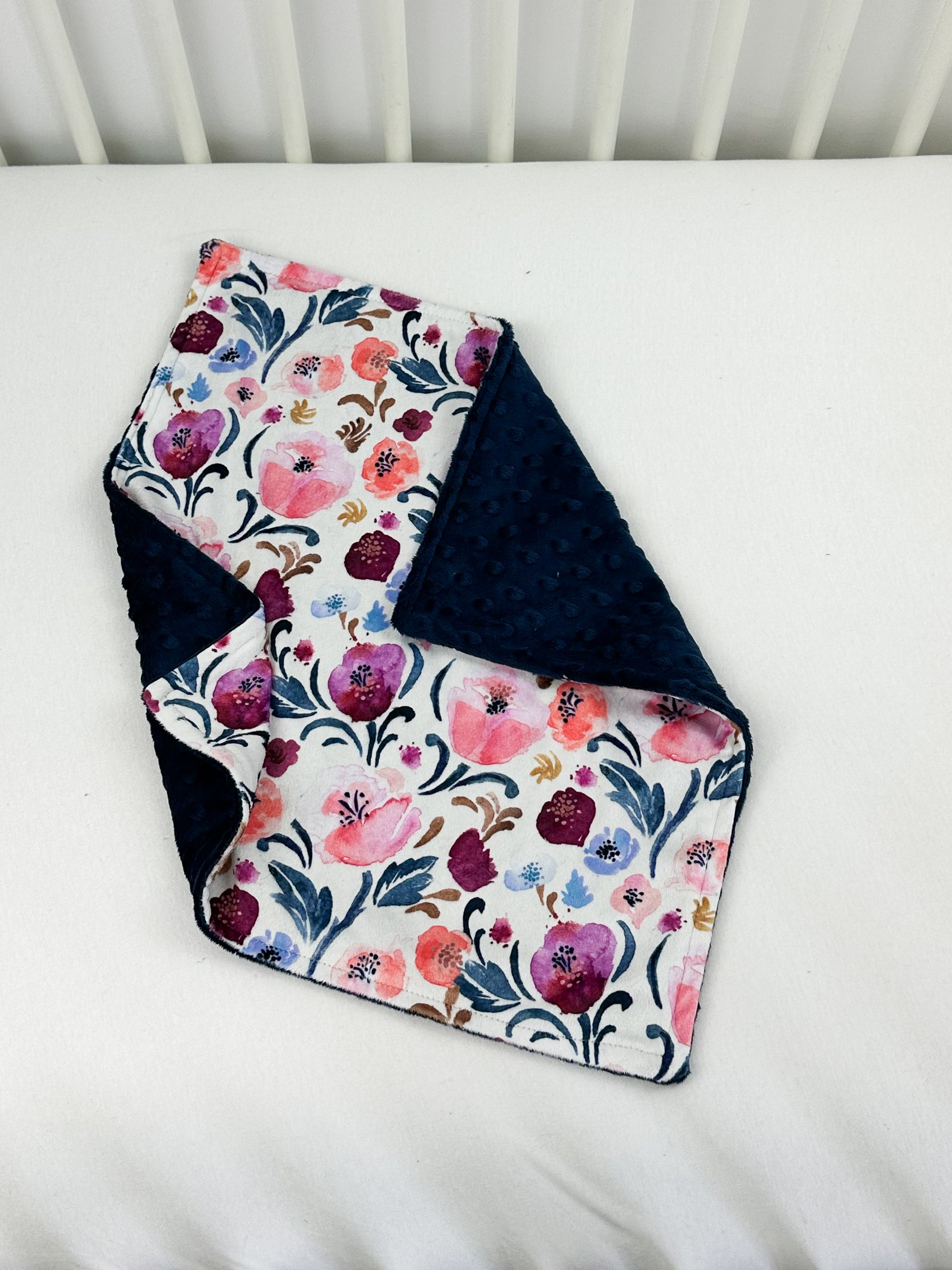 a white crib with a blue and pink blanket on it