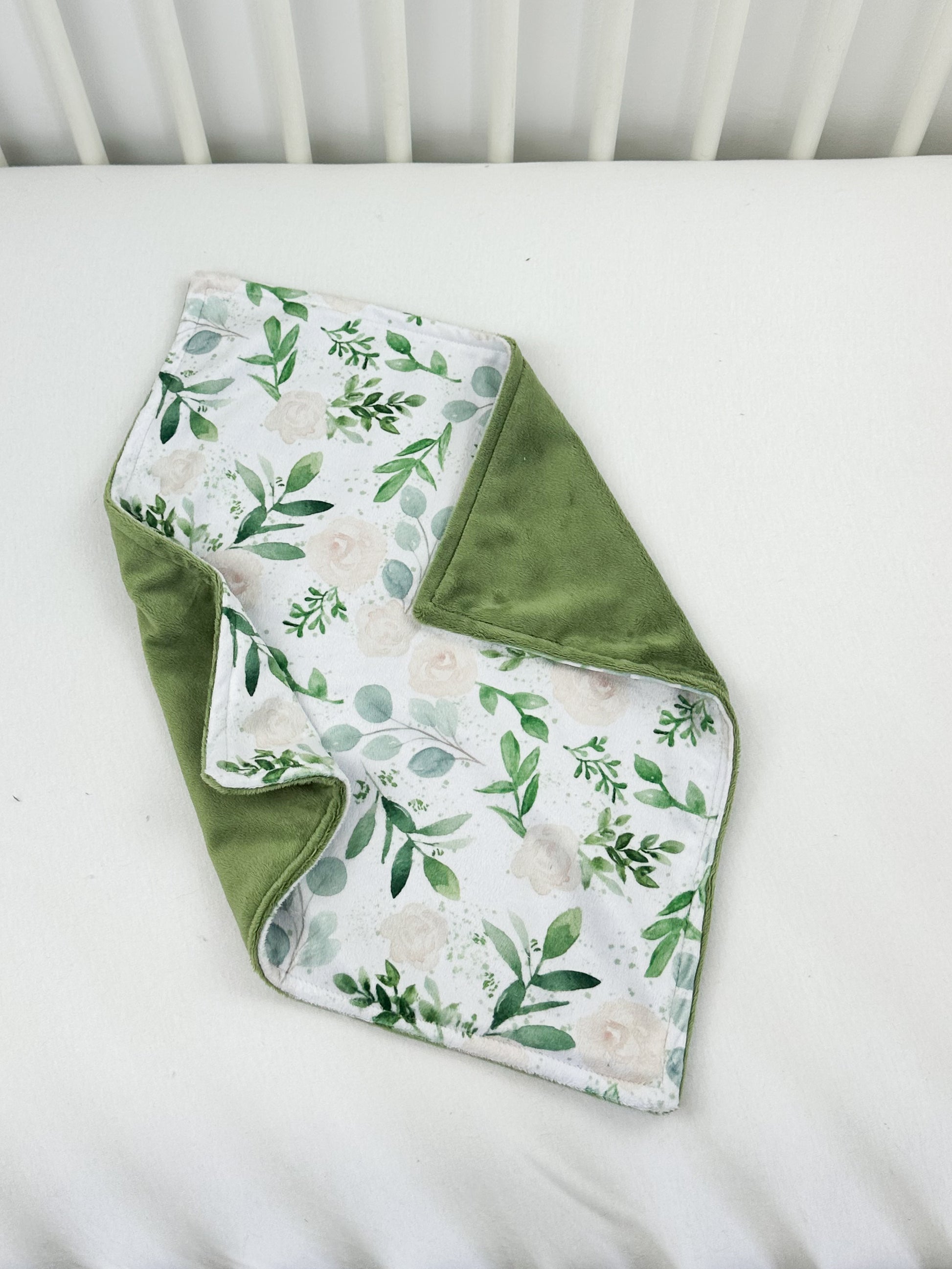 a green and white blanket laying on top of a white crib