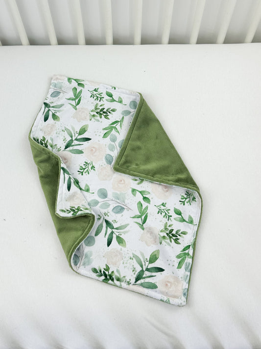a green and white blanket laying on top of a white crib