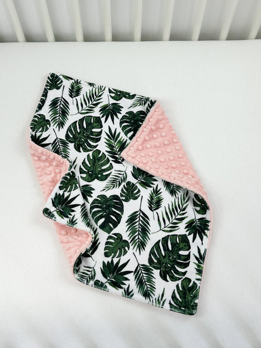 a white crib bed with a pink and green blanket