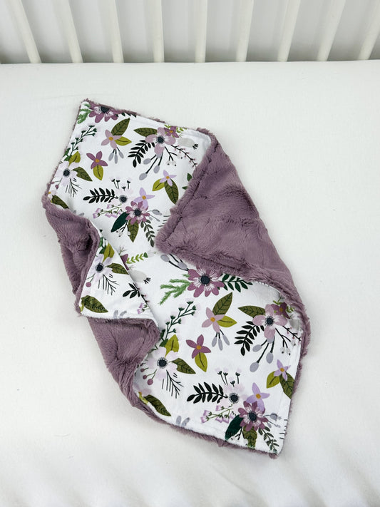 a white crib with a purple flowered blanket on top of it