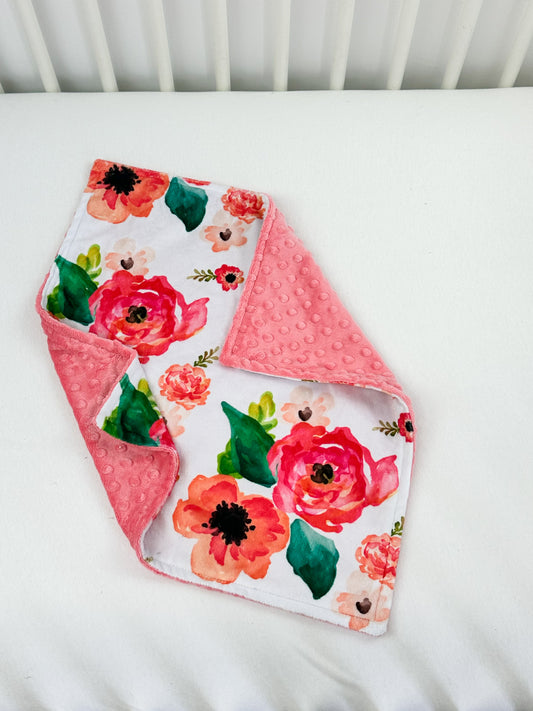 a white crib with a pink and red flowered blanket