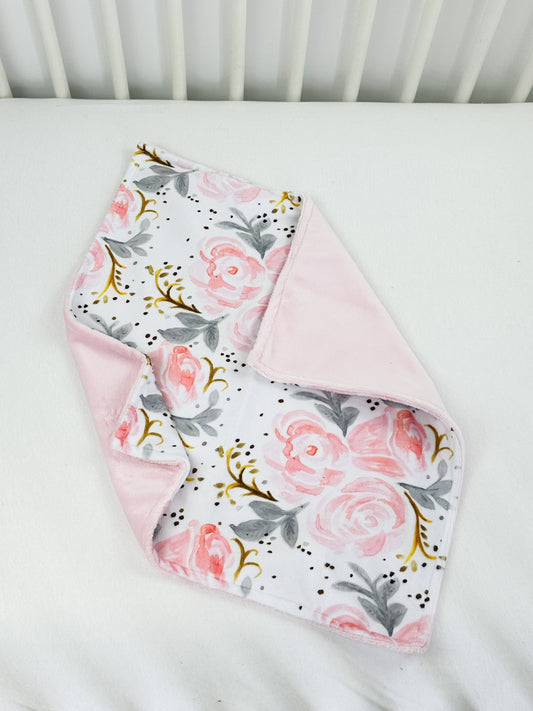 a pink and gray floral blanket on top of a white crib