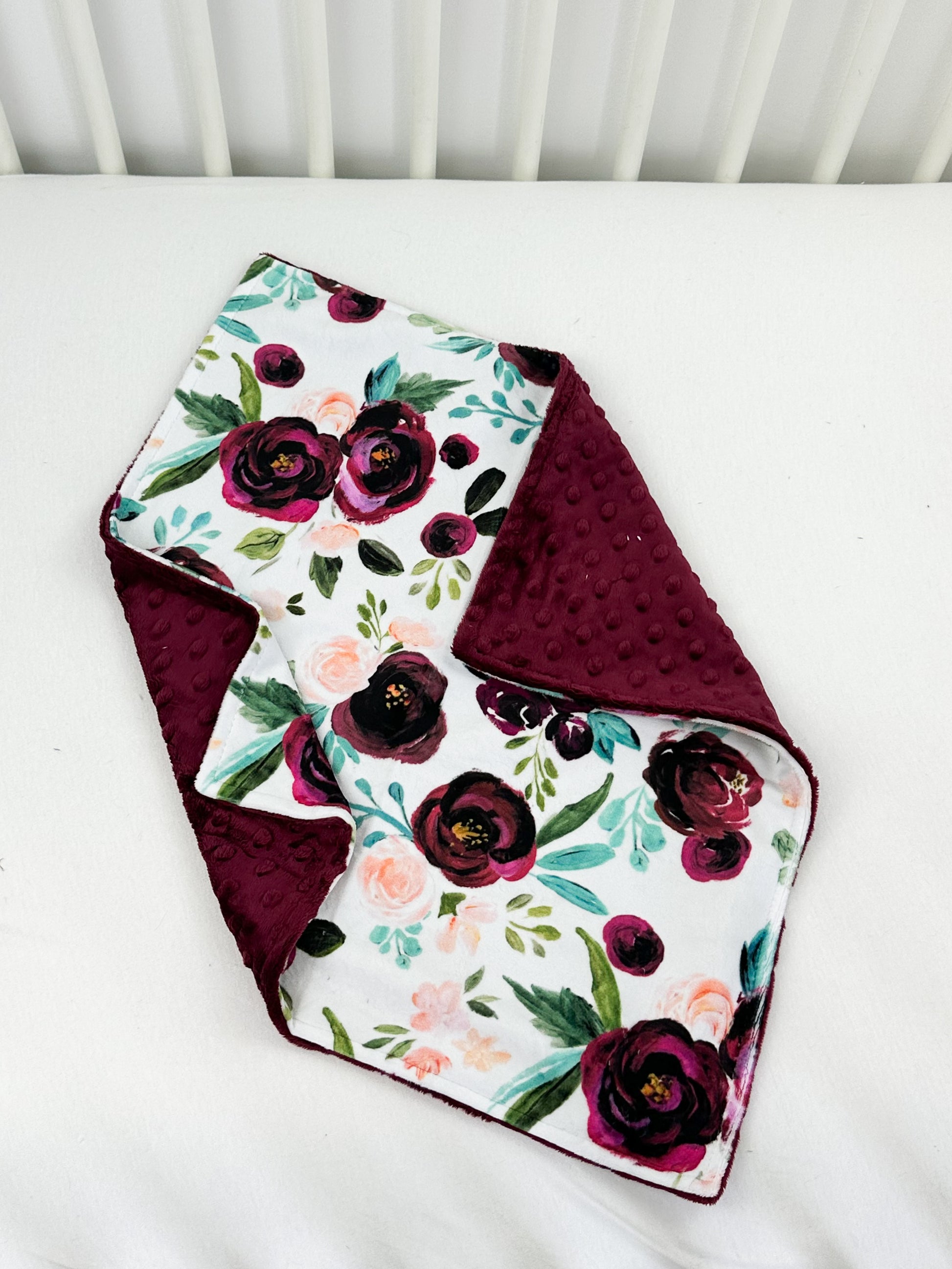 a white crib with a red and purple flowered blanket on top of it