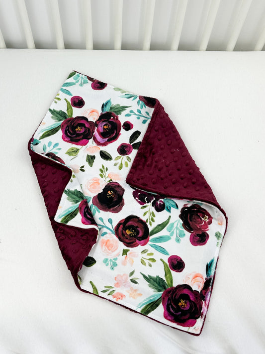 a white crib with a red and purple flowered blanket on top of it