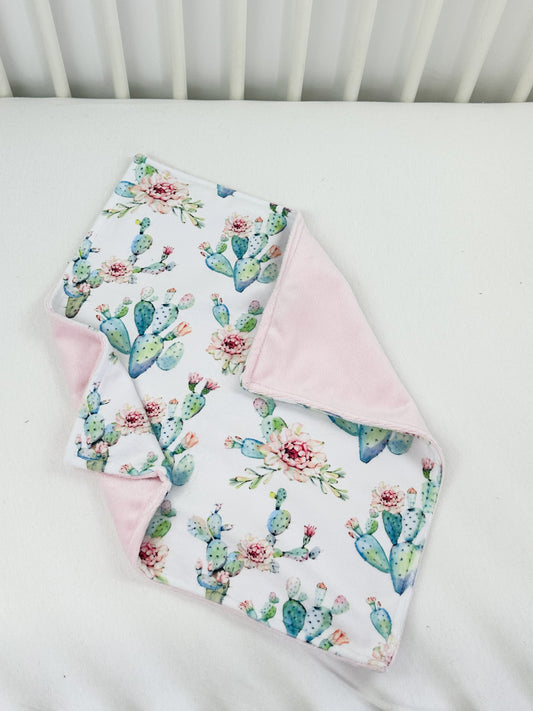 a white crib with a pink blanket and a cactus print blanket